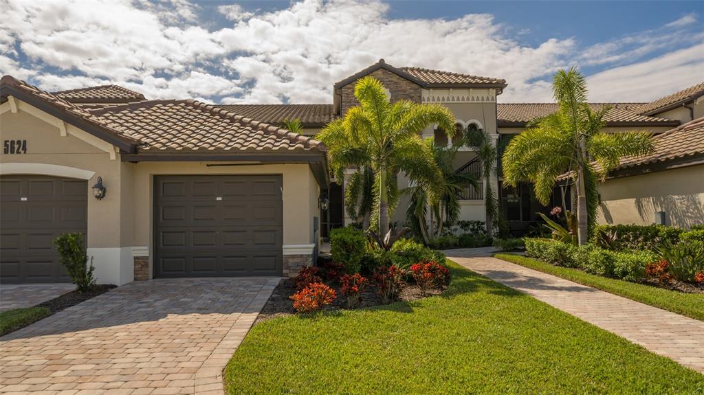 A beige two-story house with a tiled roof, two garage doors, and a landscaped yard — 5624 PALMER CIRCLE UNIT 203, BRADENTON, FL