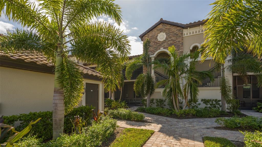 A two-story building with stone accents, a tiled roof, and palm trees along a walkway — 5624 PALMER CIRCLE UNIT 203, BRADENTON, FL