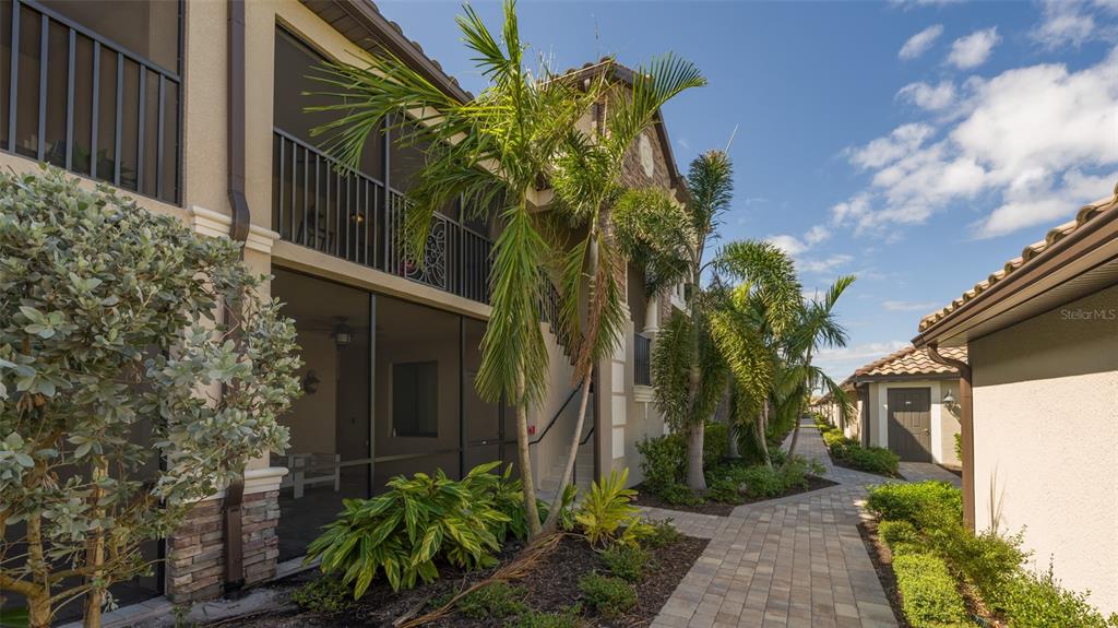 A paved walkway leads past a multi-story apartment building with screened balconies and palm trees — 5624 PALMER CIRCLE UNIT 203, BRADENTON, FL