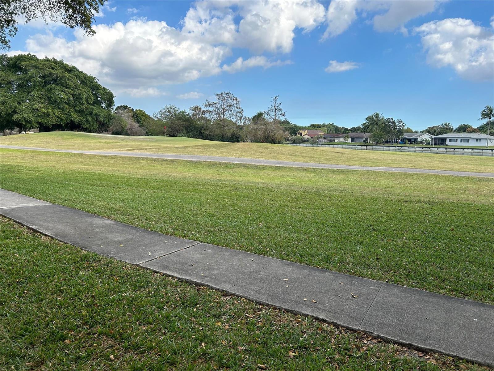A view of a grassy golf course fairway with a paved path and distant houses — 9080 Lime Bay Boulevard # 305, Tamarac FL 33312, TAMARAC, FL