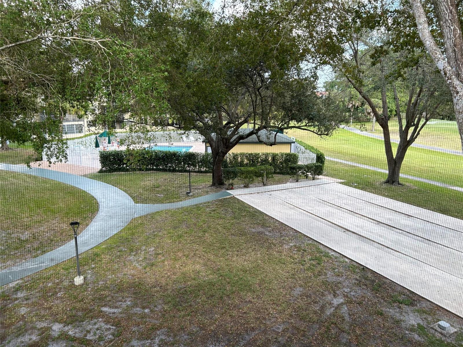An elevated view of a grassy lawn, a concrete walkway, and a fenced swimming pool — 9080 Lime Bay Boulevard # 305, Tamarac FL 33312, TAMARAC, FL