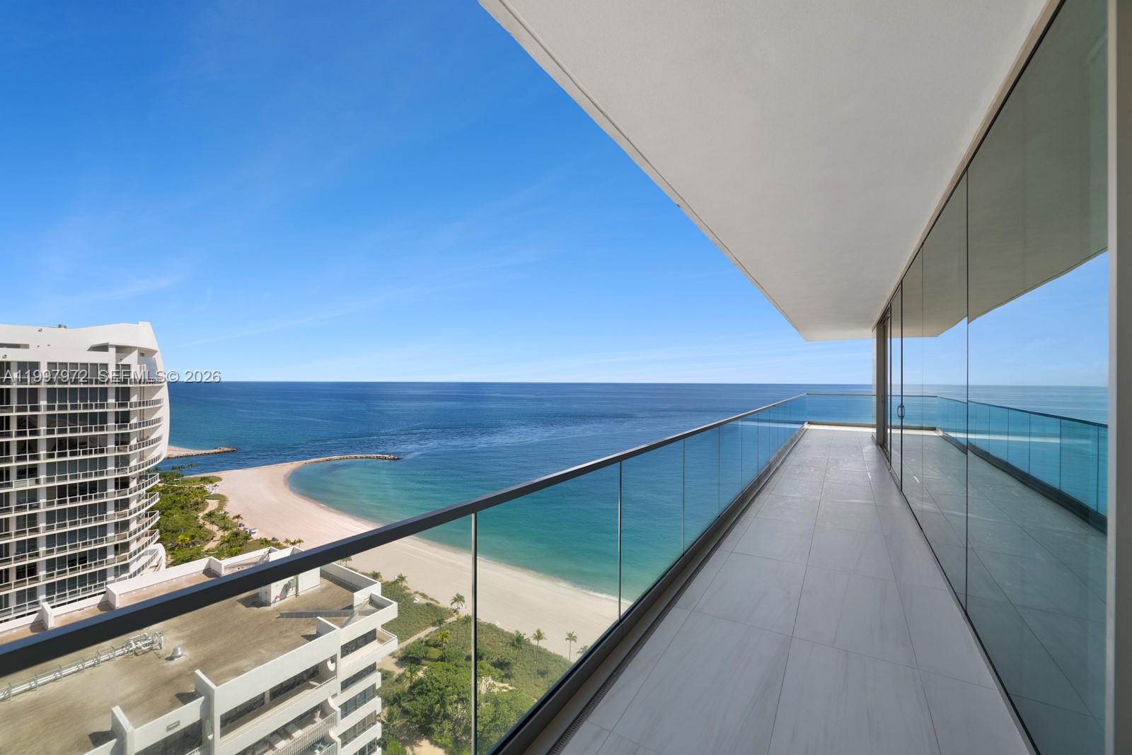 A balcony with glass railings overlooks a beach, ocean, and neighboring high-rise buildings — 10203 Collins Ave # 1001, Bal Harbour FL 33154, BAL HARBOUR, FL