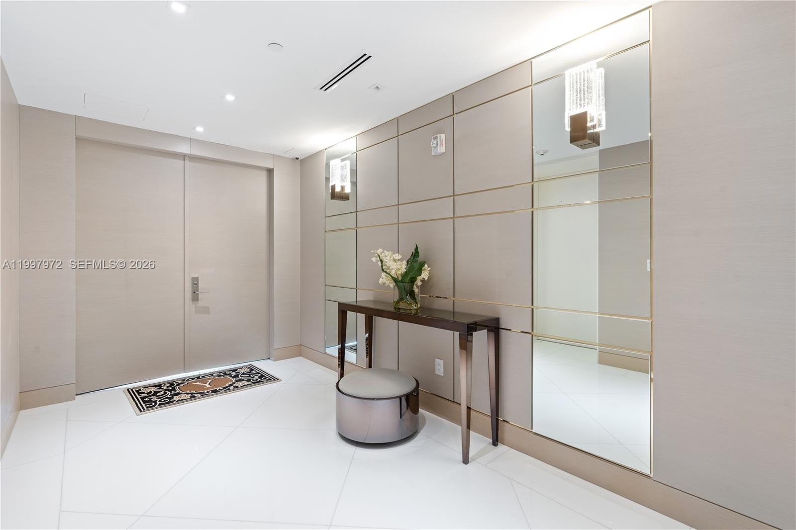 A modern entryway features a console table, ottoman, mirrored wall panels, and white tile flooring — 10203 Collins Ave # 1001, Bal Harbour FL 33154, BAL HARBOUR, FL