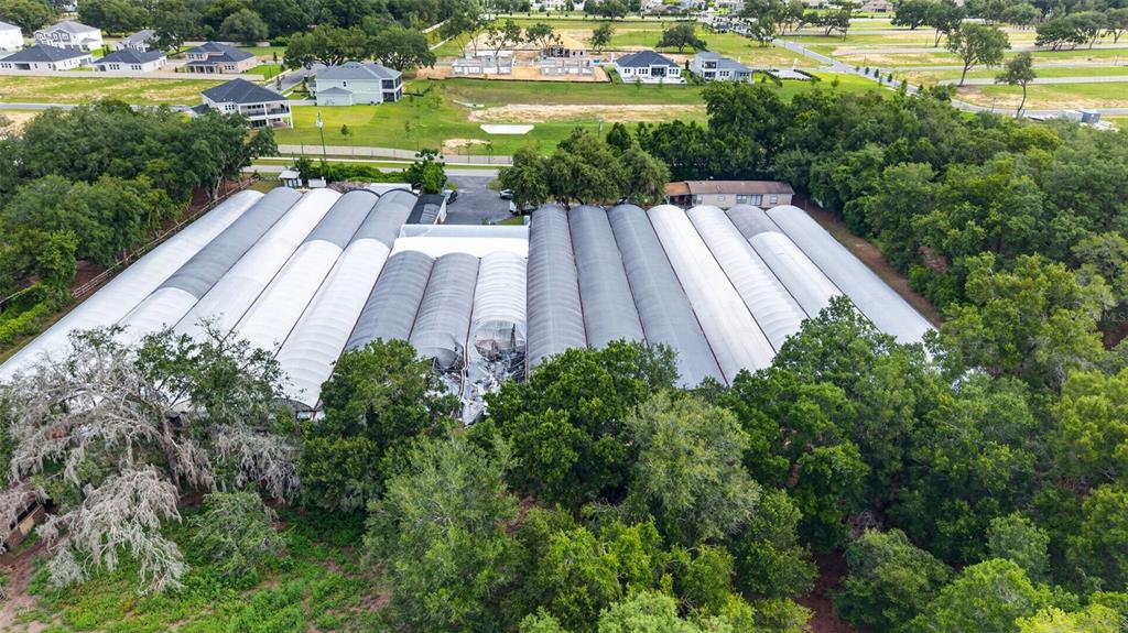 An aerial view shows a large greenhouse complex with damaged roof panels near dense trees — 2866 LENT ROAD, APOPKA, FL