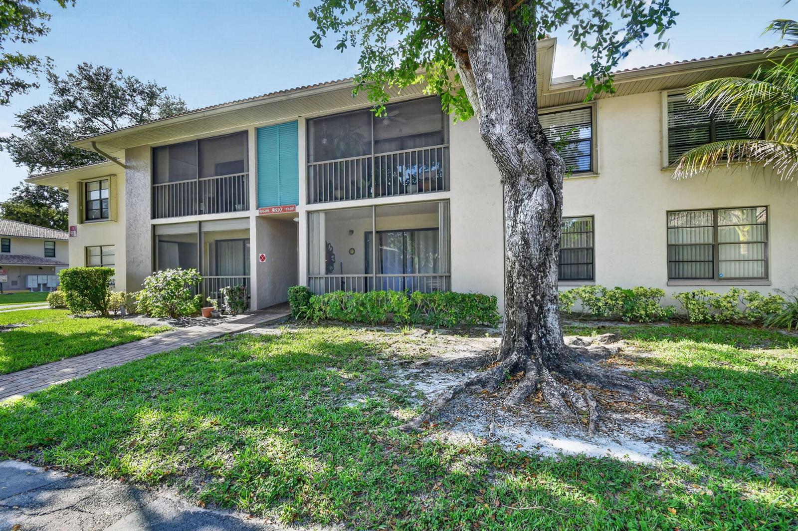 A two-story apartment building features screened balconies, a large tree, and a paved walkway — 9810 Pineapple Tree, Drive # 103, Boynton Beach FL 33436, BOYNTON BEACH, FL