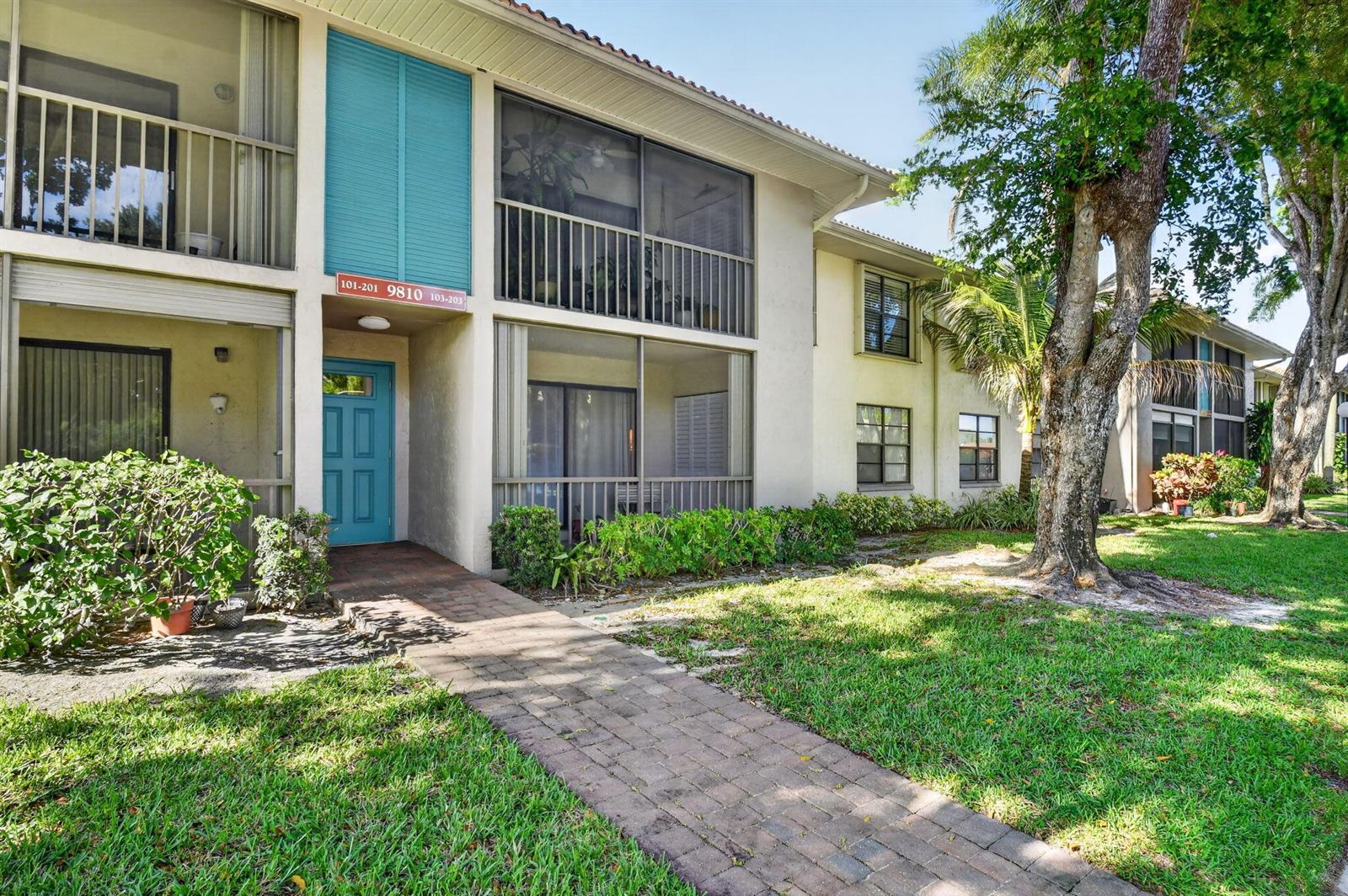 A two-story apartment building features a brick walkway leading to a blue front door — 9810 Pineapple Tree, Drive # 103, Boynton Beach FL 33436, BOYNTON BEACH, FL