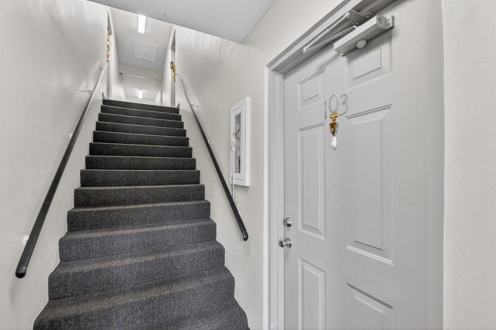 A carpeted staircase leads upward next to a gray door labeled 103 — 9810 Pineapple Tree, Drive # 103, Boynton Beach FL 33436, BOYNTON BEACH, FL