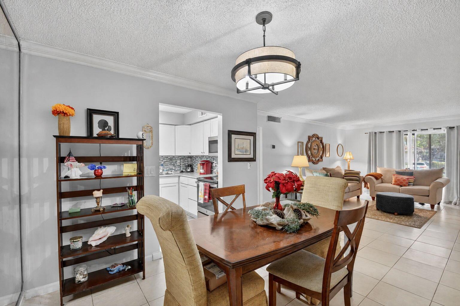 A dining area with a wooden table and chairs sits adjacent to a kitchen and living room — 9810 Pineapple Tree, Drive # 103, Boynton Beach FL 33436, BOYNTON BEACH, FL