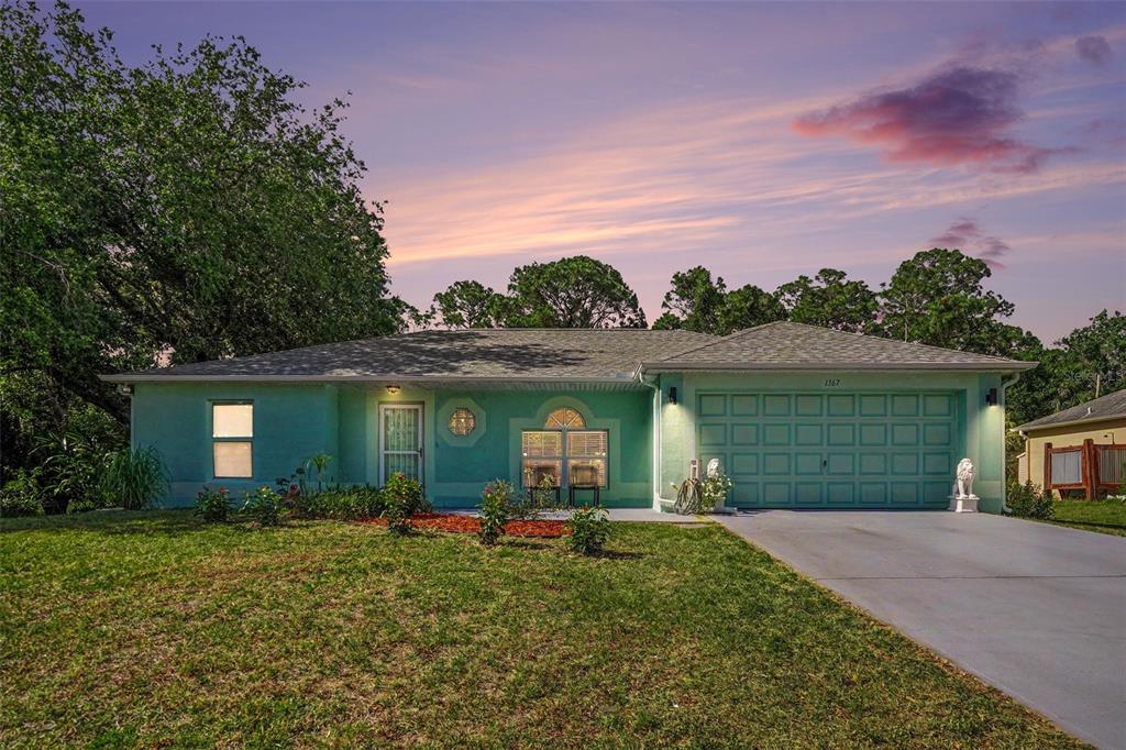 A single-story light green house with a two-car garage and a paved driveway at dusk — 1367 WING ROAD SW, PALM BAY, FL