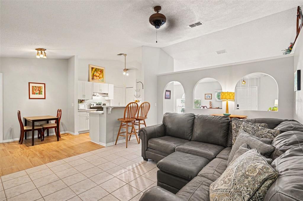 A living room features a large brown sectional sofa, a television on a wooden stand, and tile flooring — 1367 WING ROAD SW, PALM BAY, FL