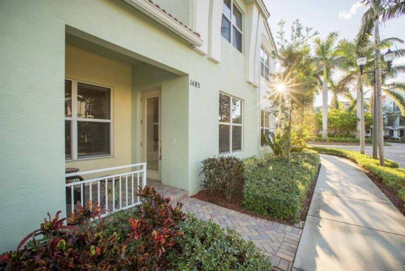 A light green two-story townhouse exterior features a covered entryway, white railing, and brick walkway — 1485 NW 48th Drive, Boca Raton FL 33431, BOCA RATON, FL