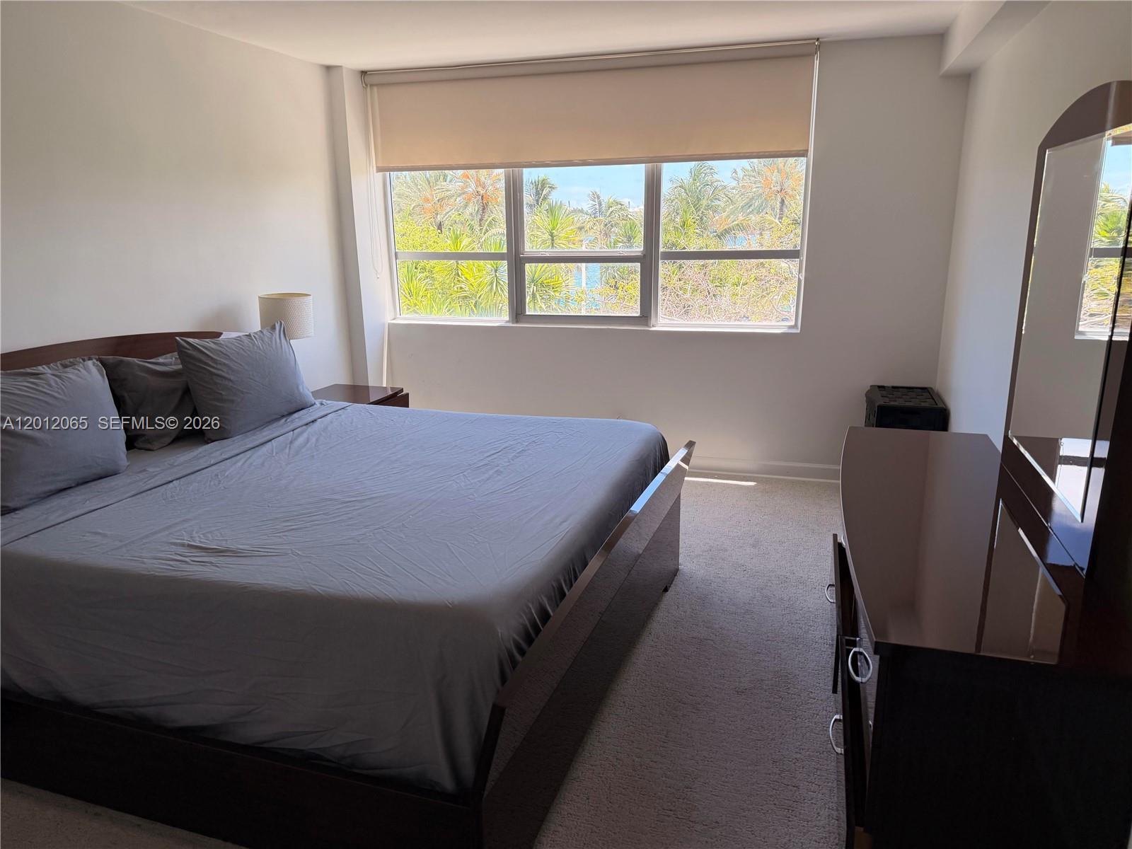 A bedroom features a dark wood bed frame, gray bedding, and a window with palm trees — 1500 Bay Rd # 318S, Miami Beach FL 33139, MIAMI BEACH, FL