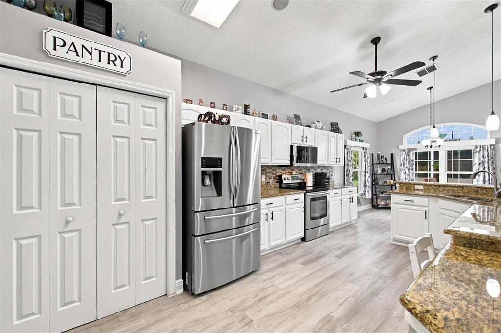 A kitchen features white cabinets, stainless steel appliances, granite countertops, and light wood-look flooring — 919 ASHTON DR, DAVENPORT, FL