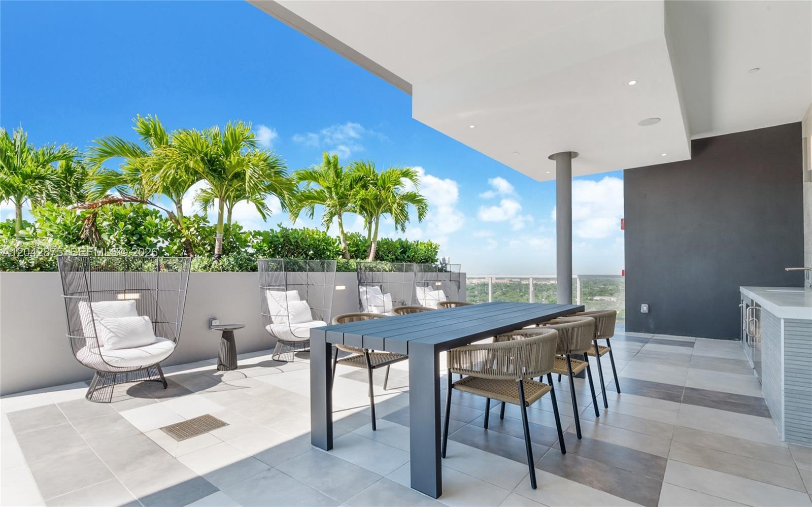 A modern outdoor balcony features a dining table, lounge chairs, and a built-in kitchen area — 9600 S Dixie Hwy # S1, Miami FL 33156, MIAMI, FL