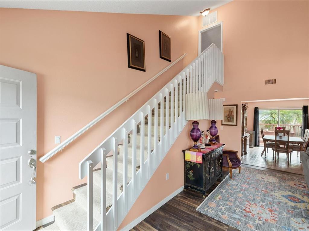 An entryway features a white staircase, peach walls, a dark wood floor, and a patterned rug — 3910 77TH PLACE E, SARASOTA, FL