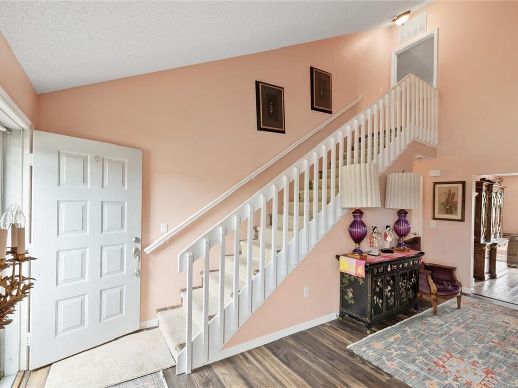 An entryway features a white staircase, peach-colored walls, and a wood-look floor — 3910 77TH PLACE E, SARASOTA, FL