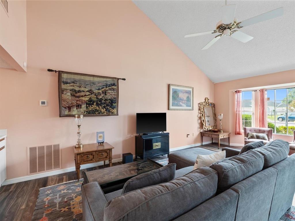 A living room with peach walls, a vaulted ceiling, a ceiling fan, and gray furniture — 3910 77TH PLACE E, SARASOTA, FL