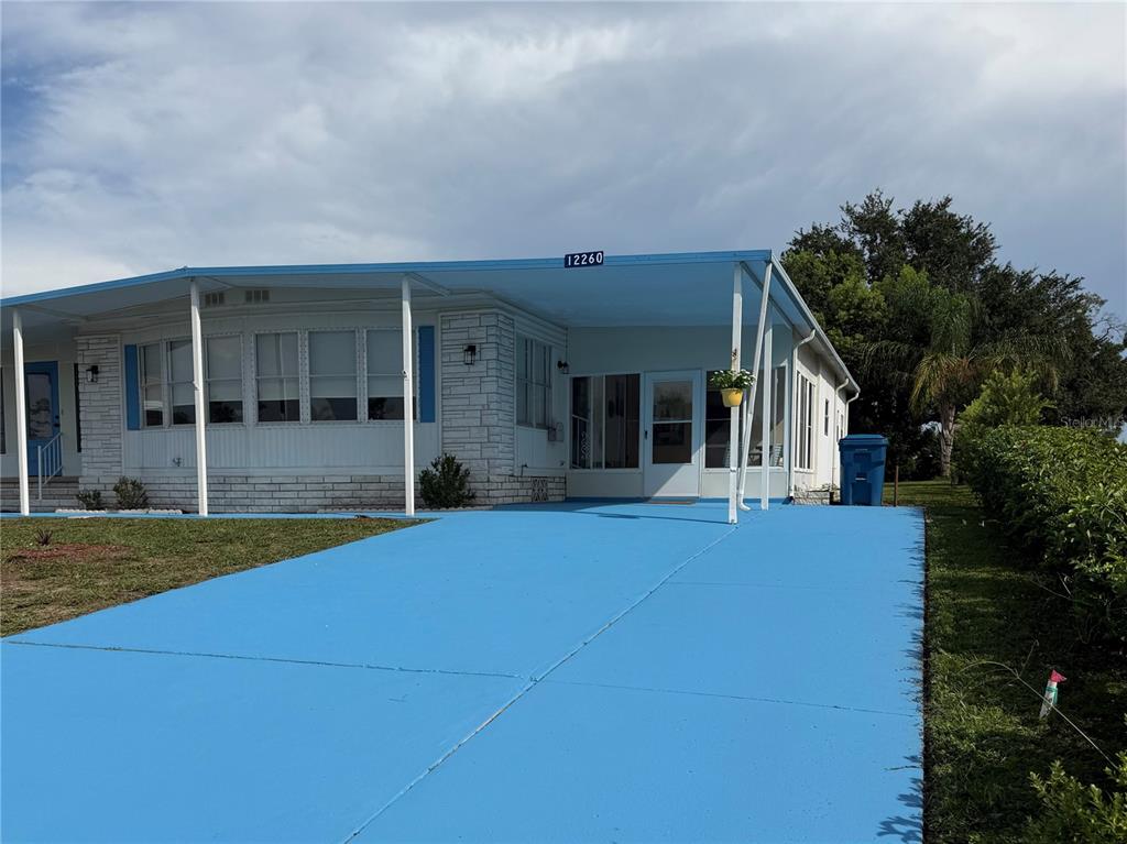 A single-story manufactured home features a bright blue painted driveway and a covered carport — 12260 HALLMARK AVENUE, BROOKSVILLE, FL