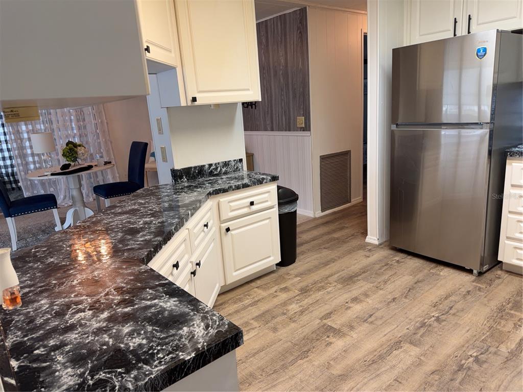 A kitchen features white cabinets, black marble-patterned countertops, stainless steel appliances, and wood-look flooring — 12260 HALLMARK AVENUE, BROOKSVILLE, FL