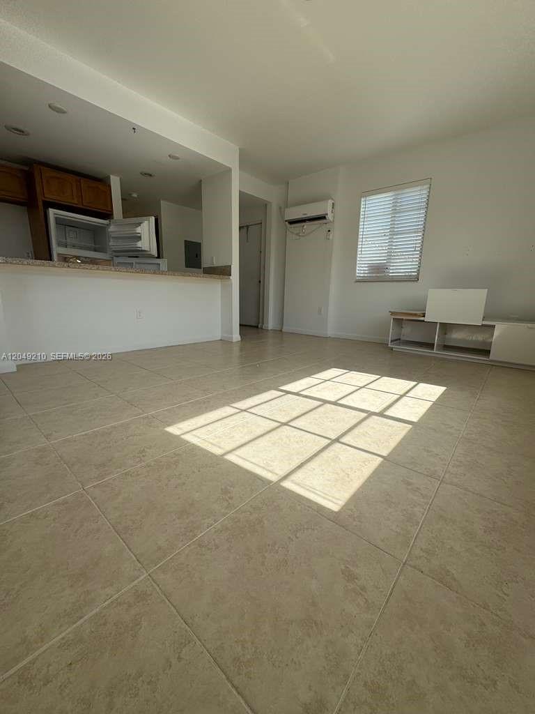 This living room features light-colored tile flooring, a kitchen pass-through, and a wall-mounted air conditioner — 7130 Rue Versailles # 6, Miami Beach FL 33141, MIAMI BEACH, FL