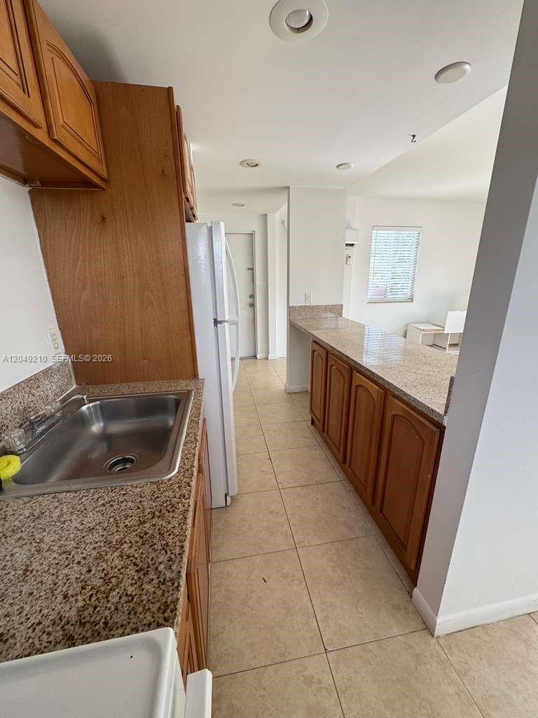 A kitchen features wooden cabinets, granite countertops, a stainless steel sink, and tile flooring — 7130 Rue Versailles # 6, Miami Beach FL 33141, MIAMI BEACH, FL