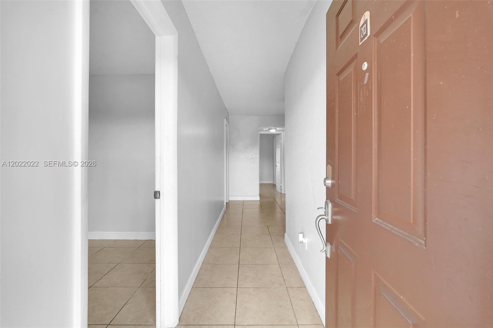 A hallway with light-colored walls and tiled flooring leads toward an open doorway — 400 NW 65th Ave # 213, Margate FL 33063, MARGATE, FL