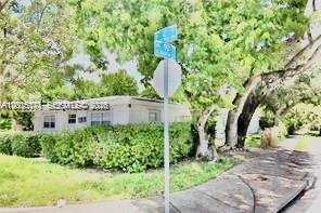 A white single-story house is partially obscured by a large tree and a street sign — EL PORTAL, FL