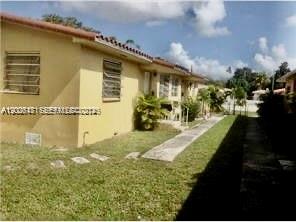 A side view of a yellow house with a concrete walkway and a grassy yard — EL PORTAL, FL