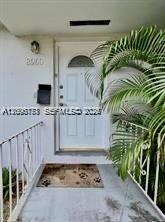 A white front door with a decorative window is accessed by a small concrete porch — EL PORTAL, FL