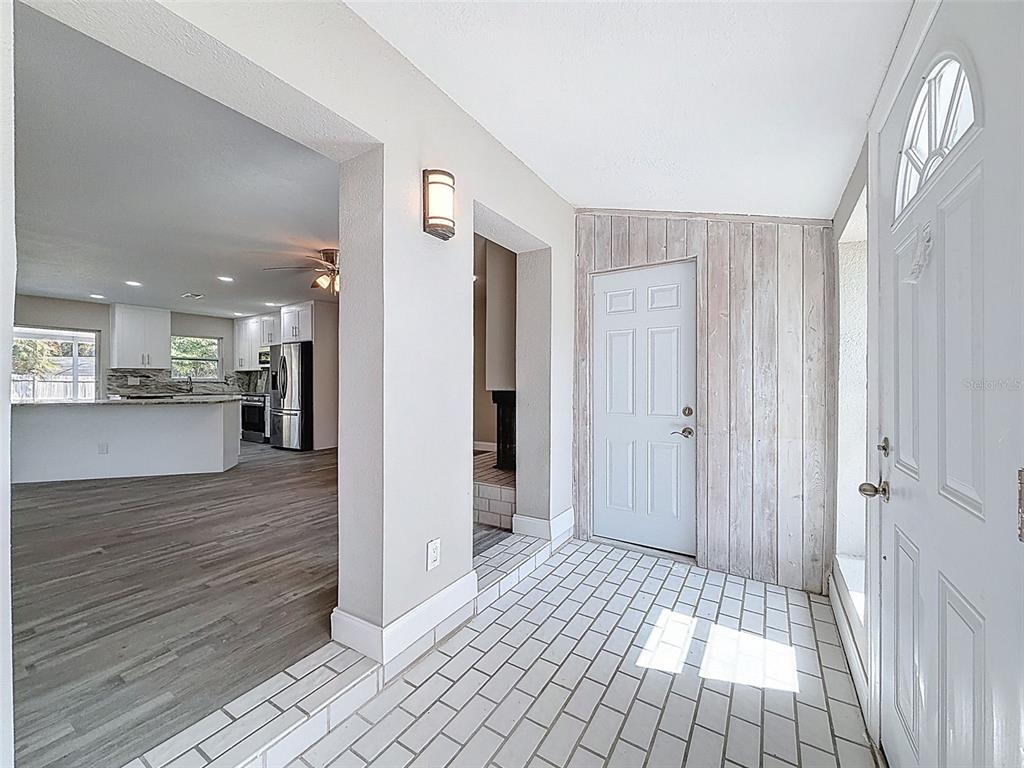 An entryway with white brick flooring, wood-paneled walls, and a view into an open kitchen — 4221 SHORE ACRES BOULEVARD NE, ST PETERSBURG, FL