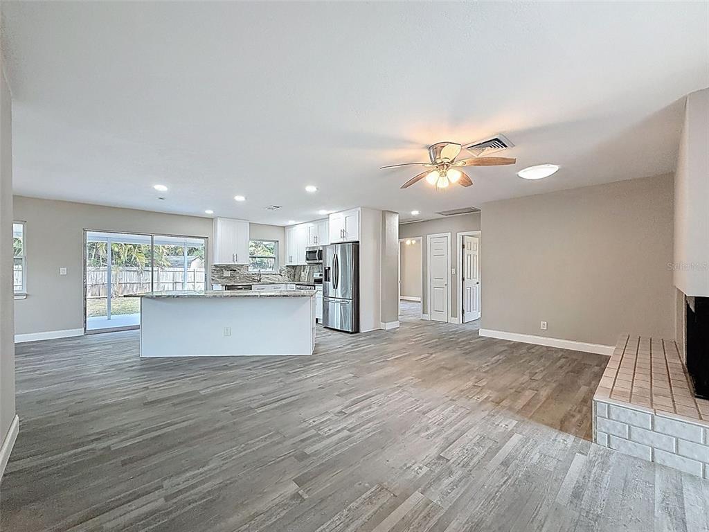 An open-concept kitchen and living area features gray wood-look flooring, white cabinetry, and stainless appliances — 4221 SHORE ACRES BOULEVARD NE, ST PETERSBURG, FL