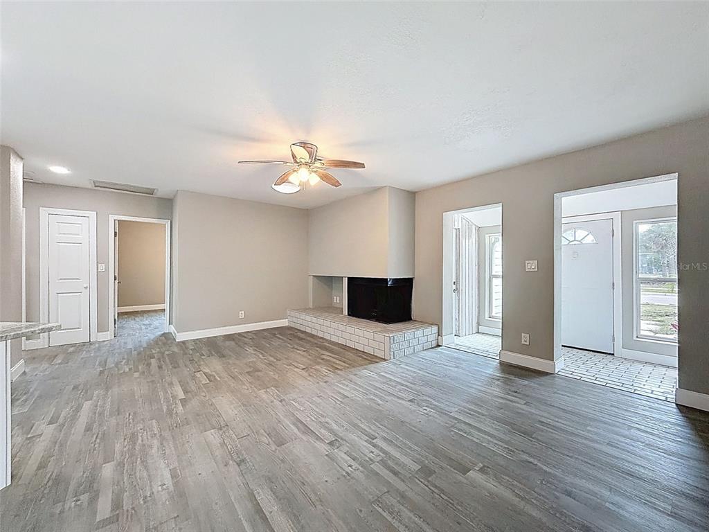 A living room features gray wood-look flooring, a brick fireplace, and an adjacent entryway — 4221 SHORE ACRES BOULEVARD NE, ST PETERSBURG, FL