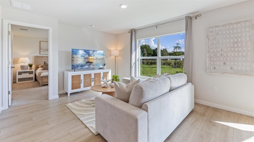 A living room features a sofa, television on a console, and a view into a bedroom — 1529 HARMON DRIVE, PORT CHARLOTTE, FL