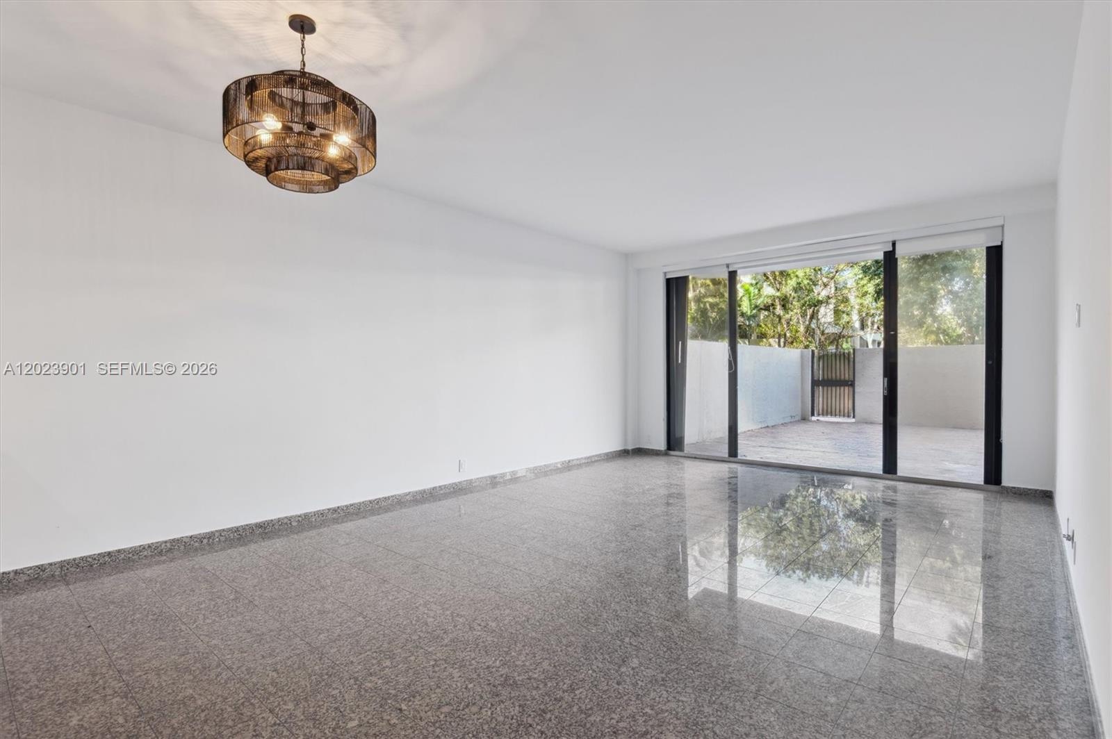 An empty room features polished granite flooring, white walls, a tiered chandelier, and sliding glass doors — 151 Crandon Blvd # 120, Key Biscayne FL 33149, KEY BISCAYNE, FL
