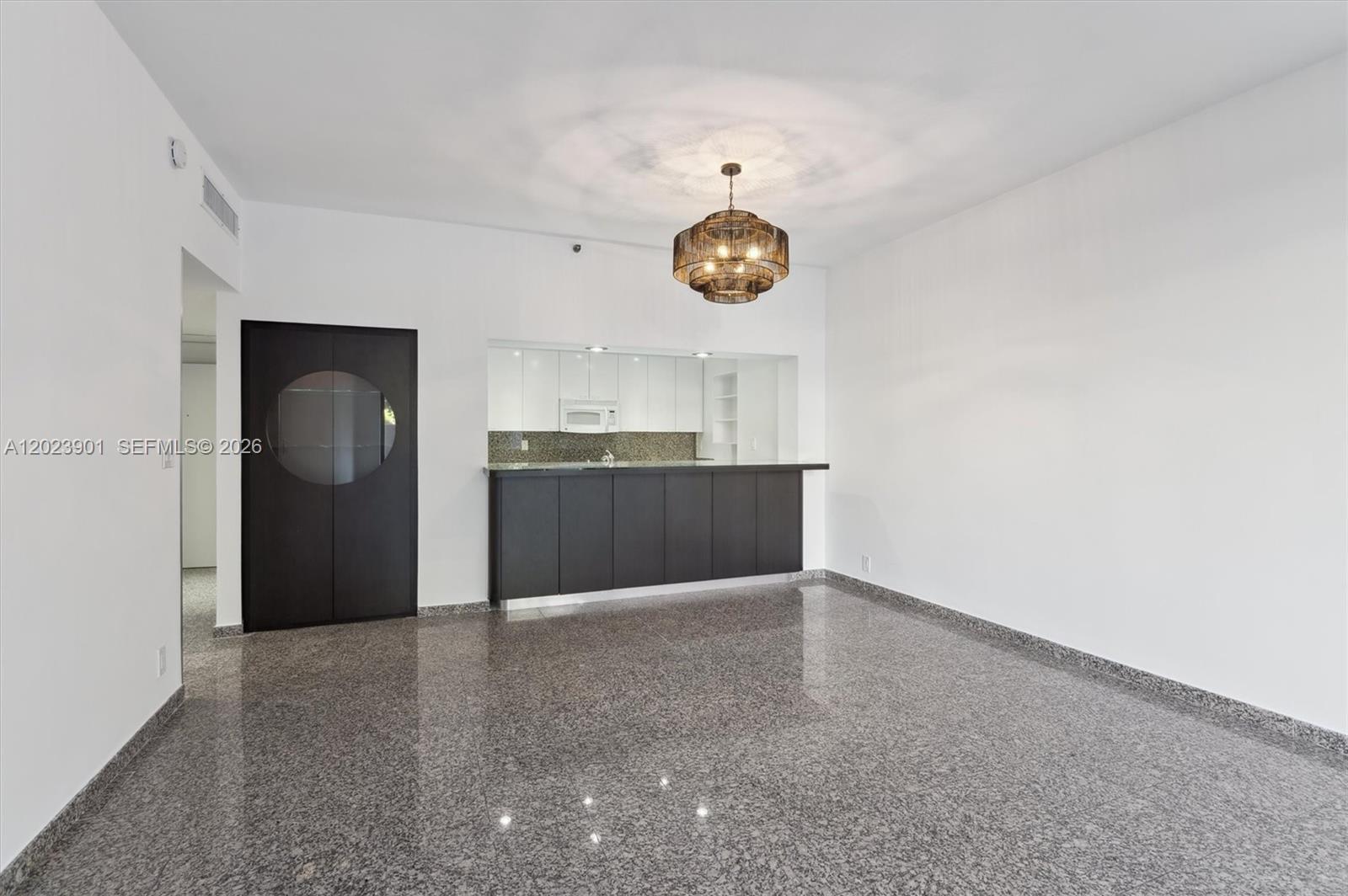 An empty room features a dark kitchen island, white cabinets, and polished granite flooring — 151 Crandon Blvd # 120, Key Biscayne FL 33149, KEY BISCAYNE, FL