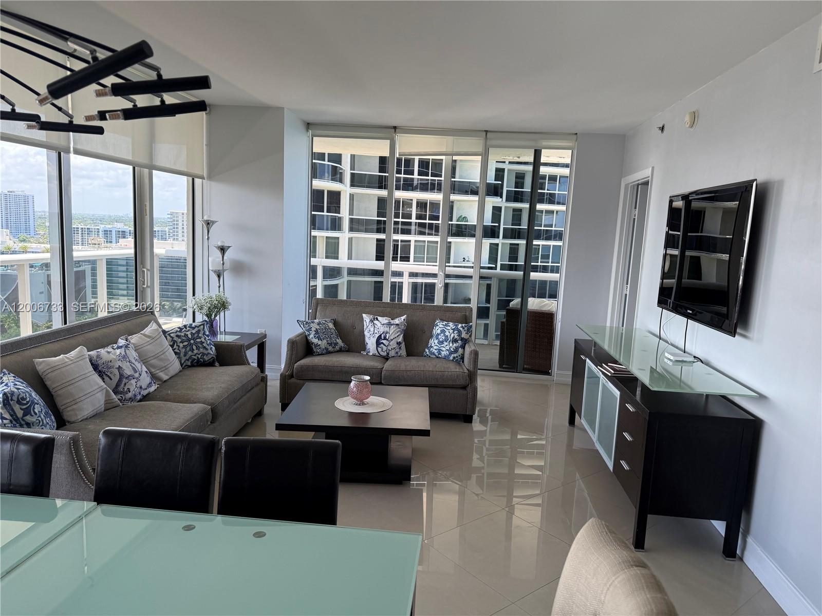 A living room features tile floors, two sofas, a glass-topped media console, and floor-to-ceiling windows — 1830 S Ocean Dr # 1708, Hallandale Beach FL 33009, HALLANDALE BEACH, FL