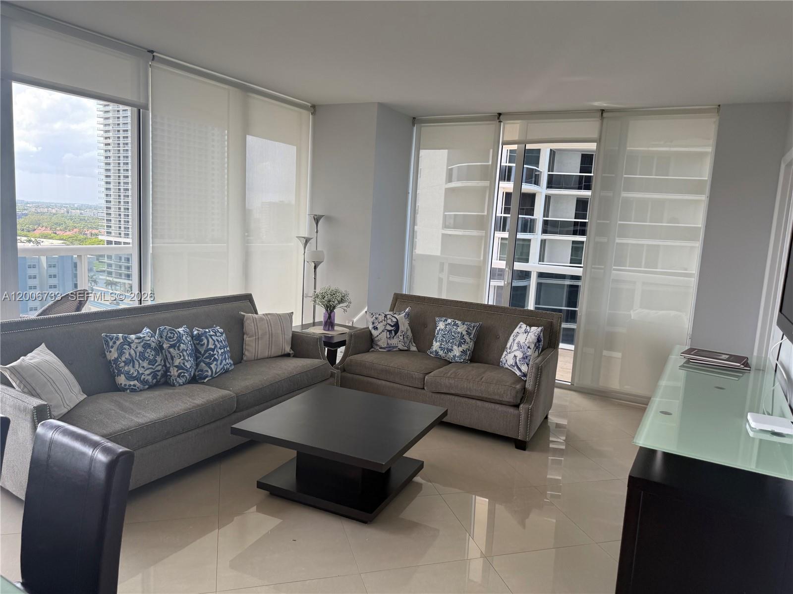 A living room features two gray sofas, a black coffee table, and floor-to-ceiling windows — 1830 S Ocean Dr # 1708, Hallandale Beach FL 33009, HALLANDALE BEACH, FL