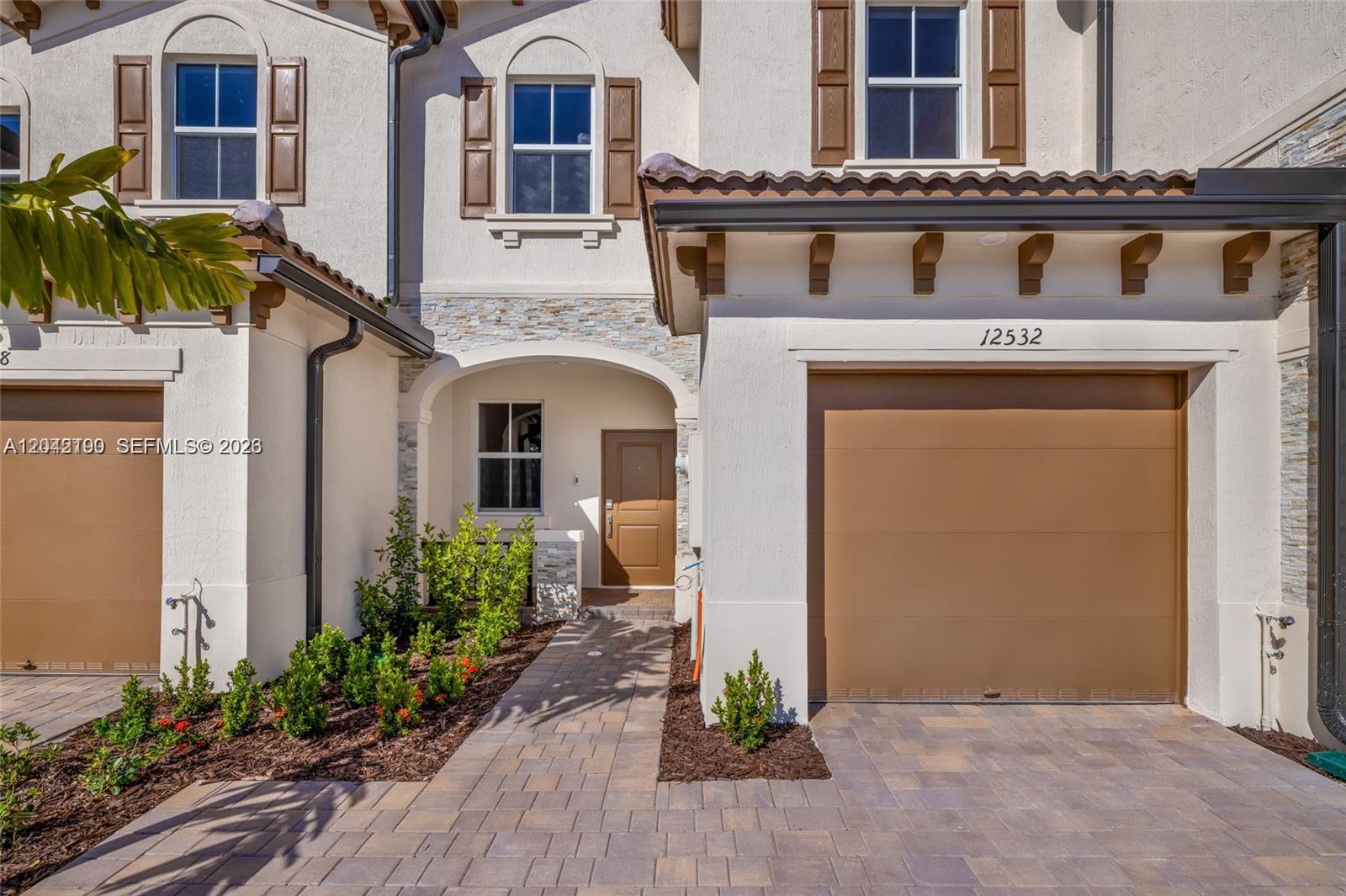 A two-story townhouse exterior features a brown garage door, arched entryway, and stone accents — 12532 NW 23rd Pl, Miami FL 33167, MIAMI, FL