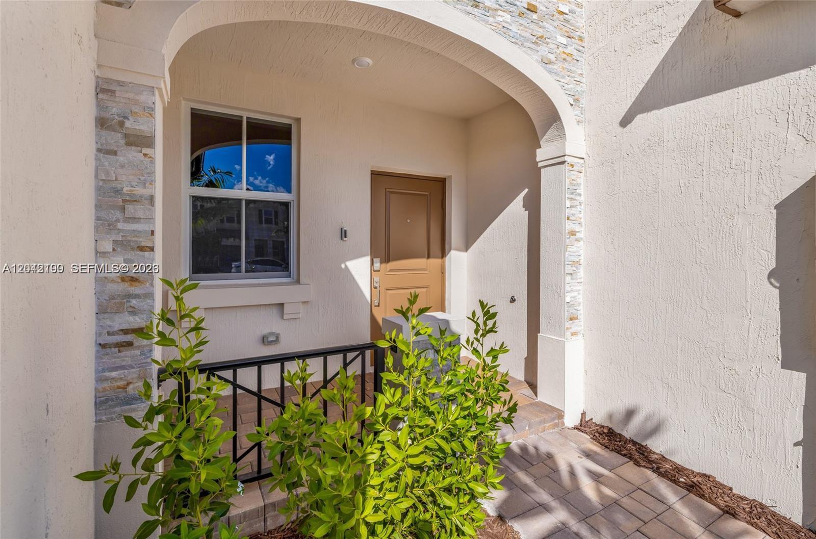 A tan front door is set within a covered entryway featuring stone accents and landscaping — 12532 NW 23rd Pl, Miami FL 33167, MIAMI, FL