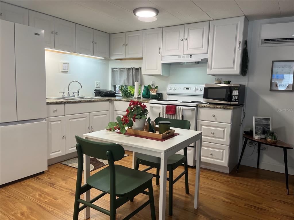 A kitchen features white cabinetry, a dining table with green chairs, and wood-look flooring — 1509 23RD AVENUE W, BRADENTON, FL