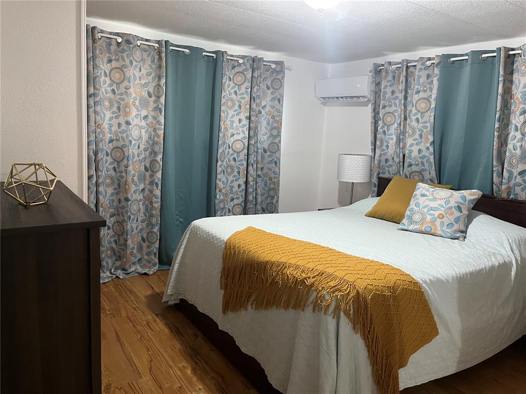 A bedroom features a bed with a yellow throw, patterned curtains, and wood-look flooring — 1509 23RD AVENUE W, BRADENTON, FL
