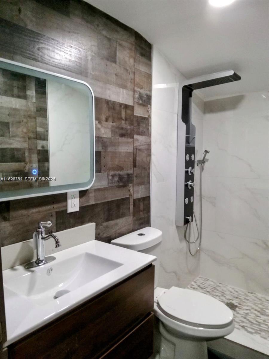 A bathroom features a wood-plank accent wall, a vanity with a mirror, and a glass-enclosed shower — 2720 NW 29th St # 2720, Miami FL 33142, MIAMI, FL