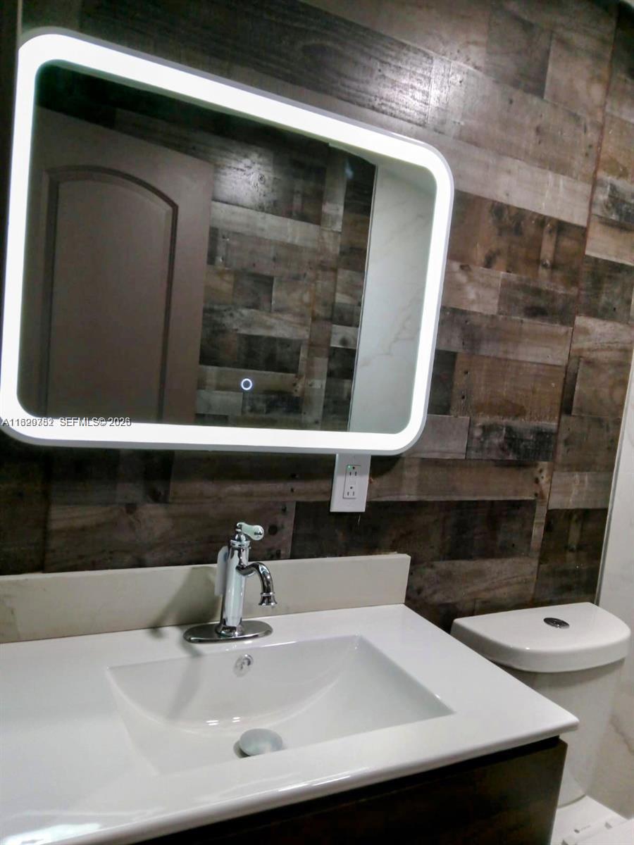 A bathroom features a vanity with a white sink, a modern LED mirror, and wood-plank walls — 2720 NW 29th St # 2720, Miami FL 33142, MIAMI, FL