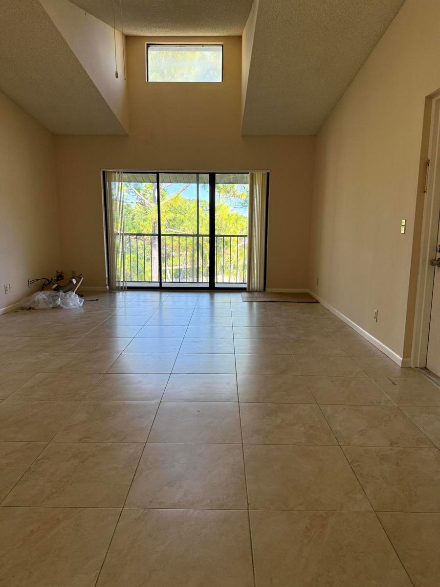 An empty room with beige tile flooring, vaulted ceilings, and a sliding glass balcony door — 703 Sunny Pine Way # B3, FL 33415, FL