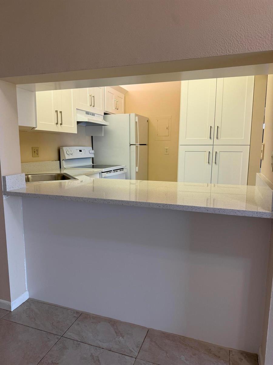 A kitchen with white cabinets, white appliances, and a light-colored stone breakfast bar — 703 Sunny Pine Way # B3, FL 33415, FL