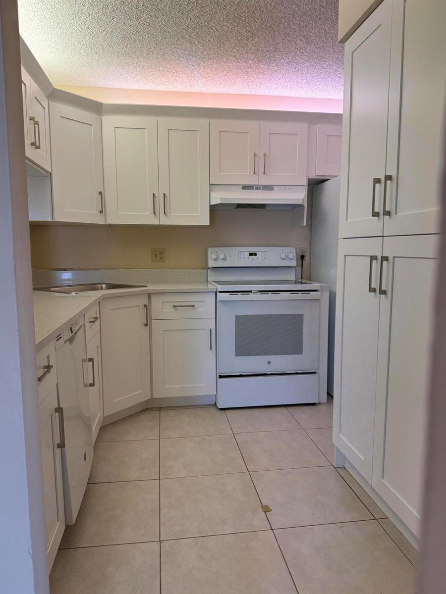 A kitchen features white cabinets, white appliances, light countertops, and beige tile flooring — 703 Sunny Pine Way # B3, FL 33415, FL