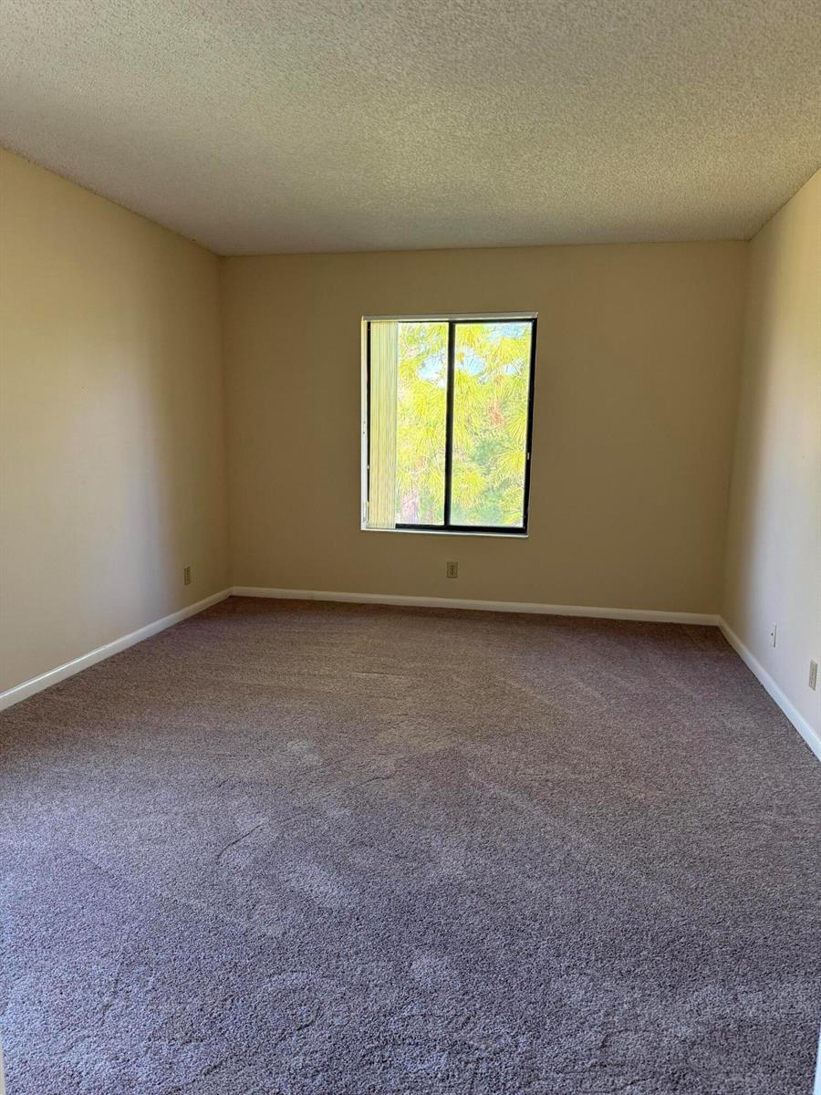 An empty room with beige walls, brown carpet, and a single window — 703 Sunny Pine Way # B3, FL 33415, FL