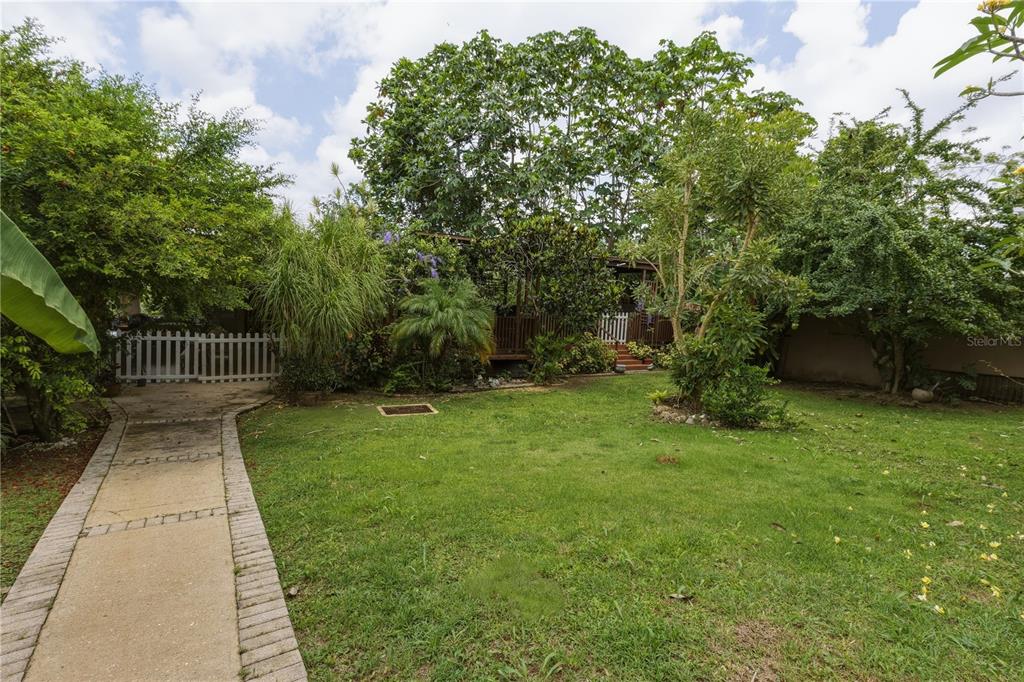 A paved walkway leads through a grassy backyard toward a wooden deck and white fence — 149 YUISA ST.  LOMAS Lot 76, MANATI, PR