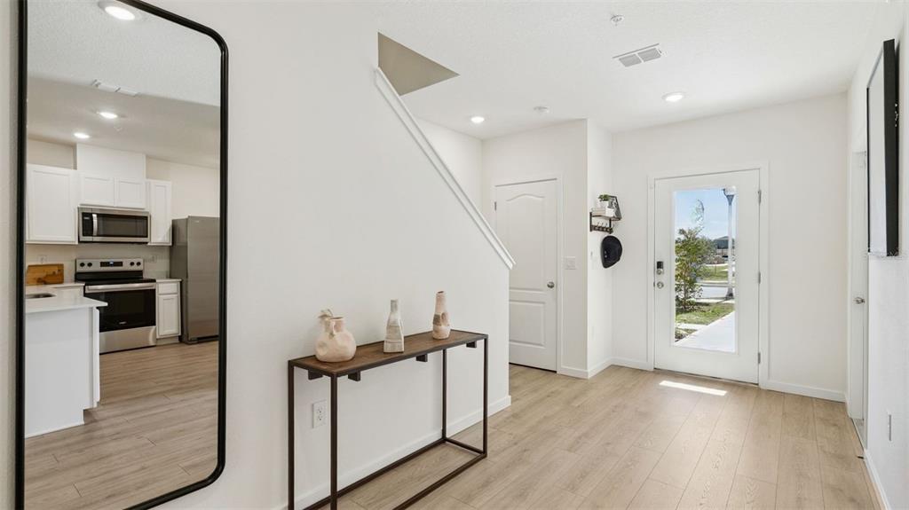 An entryway with light wood floors, a console table, a large mirror, and a kitchen — 3571 WYE OAK DRIVE, APOPKA, FL