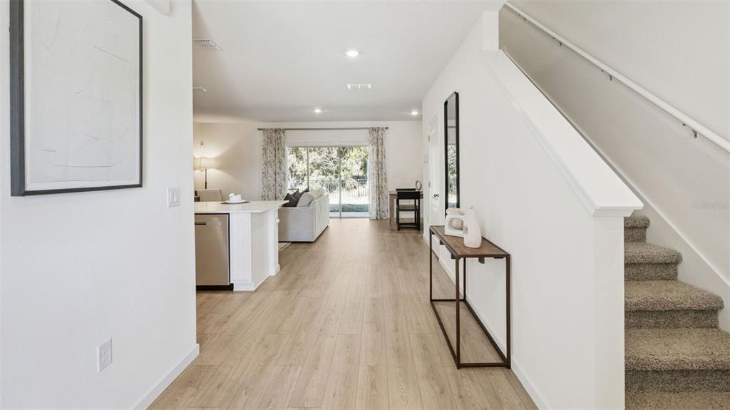 A bright, open-concept living area features light wood-look flooring, a kitchen island, and carpeted stairs — 3571 WYE OAK DRIVE, APOPKA, FL